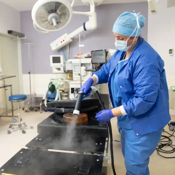 Agente en tenue de bloc désinfectant une table d'opération au nettoyeur vapeur