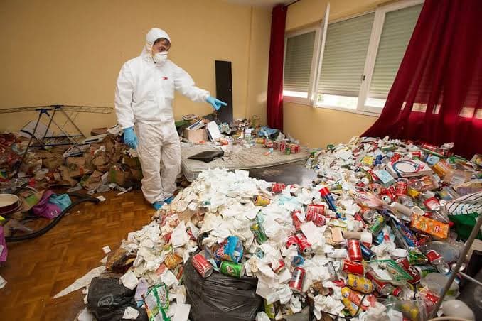 Agent en combinaison de protection dans un logement envahi de déchets